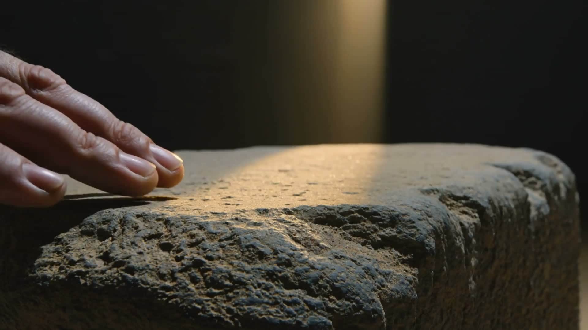 A hand resting on carved stone under a beam of light, from the AlGammal Holding brand film